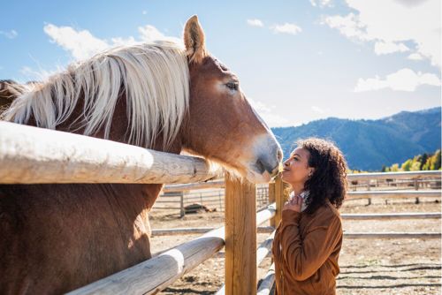Woman standing nose-to-nose with and smiling at a horse