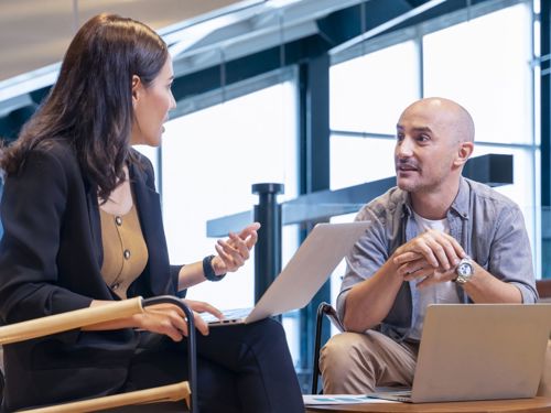 Man and woman sitting with laptops having a conversation